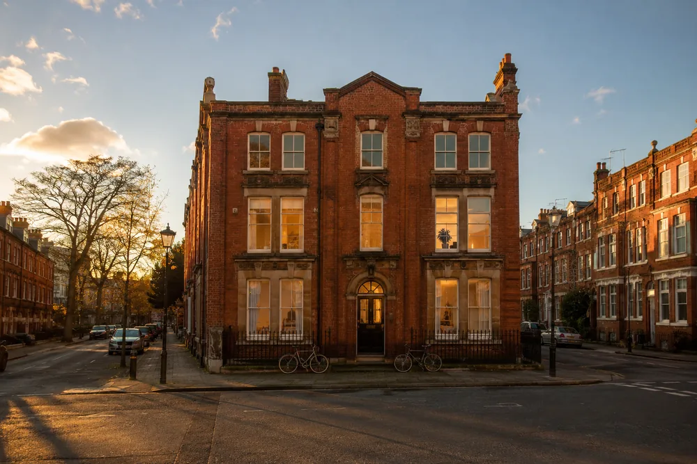 A long-vacant London commercial building with warm amber light in its windows, returning to life as community accommodation on a quiet residential street.